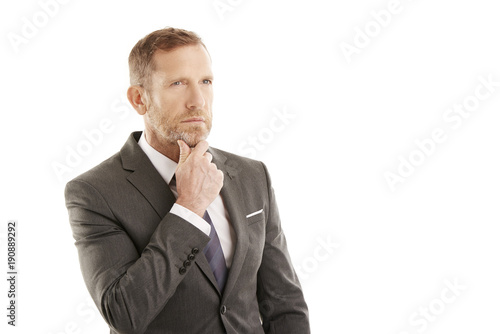 Considering the possibilities. Middle aged businessman wearing suit while standing at white background and seemd deep in thought. Professional man looking at the camera wit hands on his chin. 