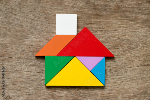 Colorful tangram puzzle in home shape on wood background