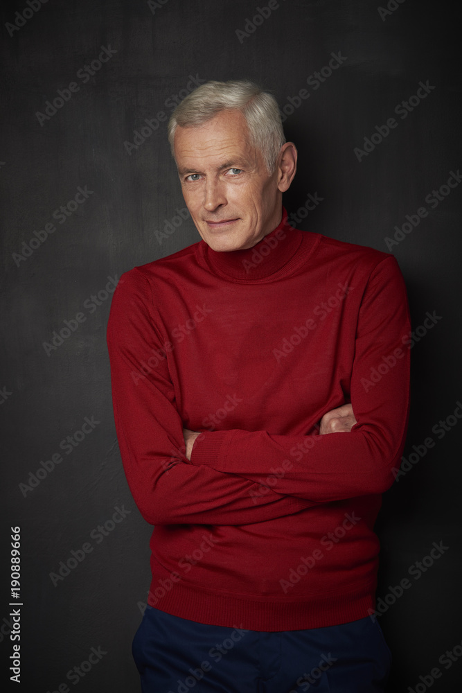 Casual senior man portrait. Handsome elderly man wearing red turtle neck sweater and looking at camera while standing against at dark background.