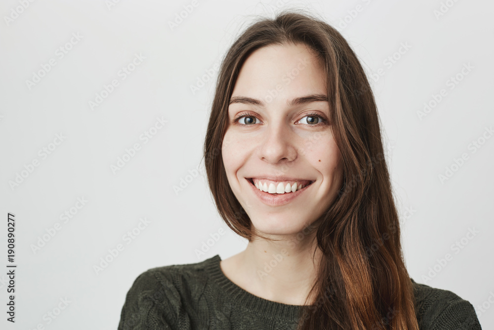 Obraz premium Close up portrait of young beautiful attractive girl, smiling cheerfully looking at camera over white background. Woman enjoys conversation with her mates, expresses positive emotions.