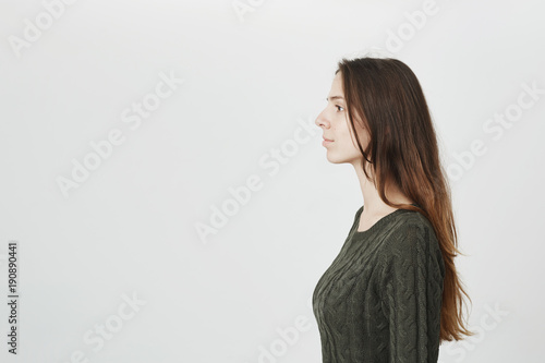 People, beauty and lifestyle concept. Profile of attractive good-looking beautiful young woman wearing knitted green sweater posing indoors. Pretty European girl standing against gray background.