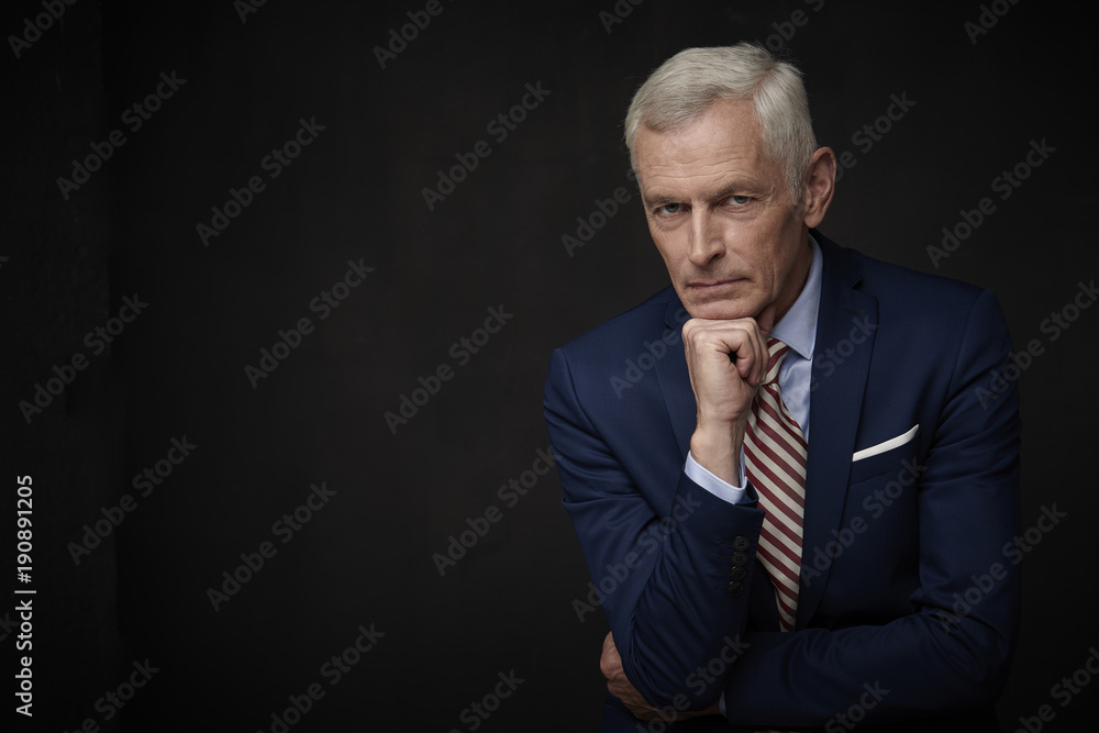 Confident businessman portrait. Executive senior lawyer businessman wearing suit and looking at camera while standing at isolated black background with copy space. Confident businessman portrait. Executive senior lawyer businessman wearing suit and looking at camera while standing at isolated black background with copy space.