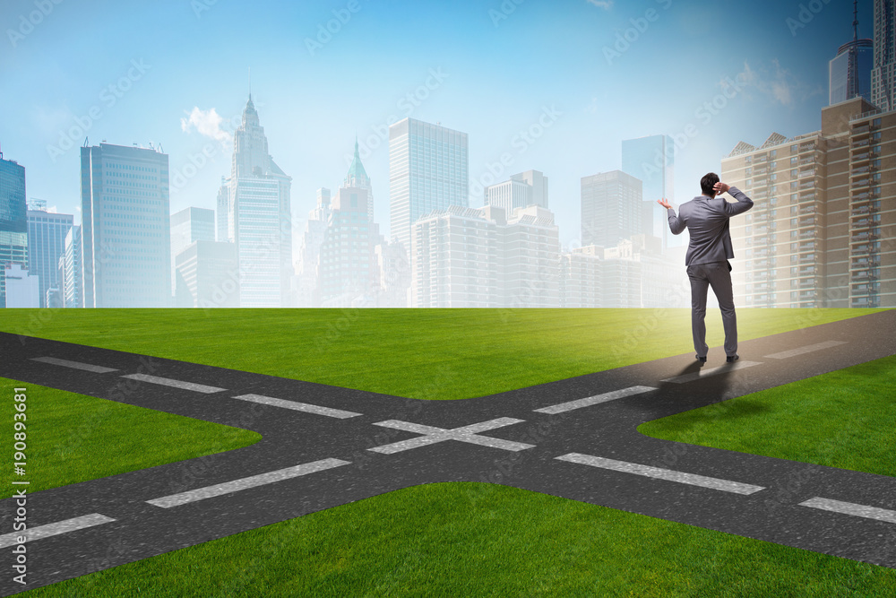 Young businessman at crossroads in uncertainty concept Young businessman at crossroads in uncertainty concept