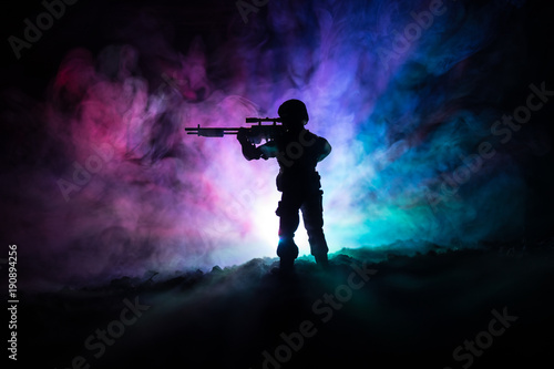 Fototapeta Naklejka Na Ścianę i Meble -  Silhouette of military sniper with sniper gun at dark toned foggy background. shot, holding gun, colorful sky, background