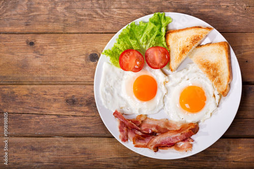 plate of fried eggs with bacon on wooden table, top view