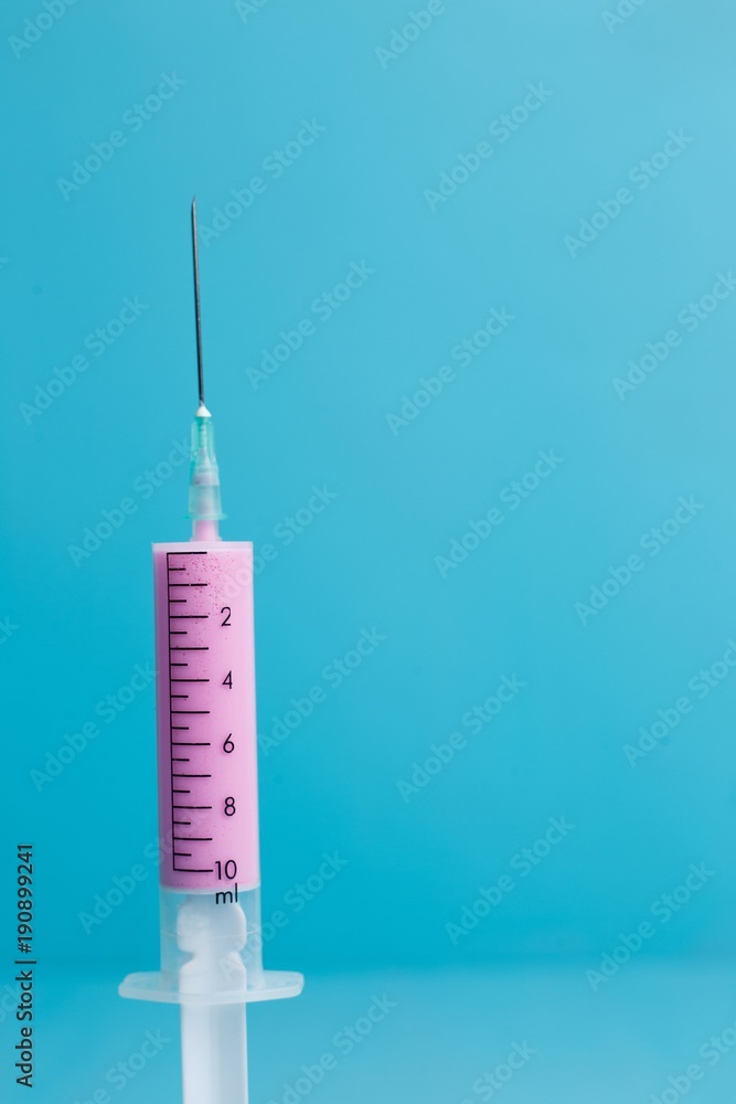 Close-up of medical syringe with pink medicine on blue background. Health care, medicine and pharmacy concept Close-up of medical syringe with pink medicine on blue background. Health care, medicine and pharmacy concept