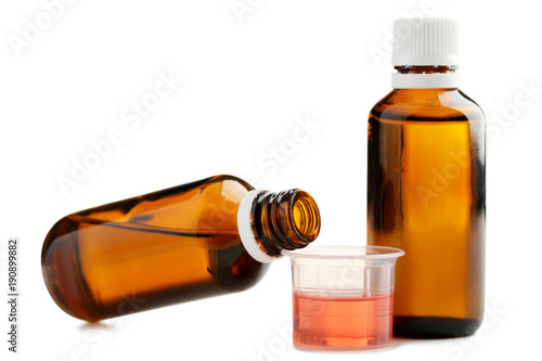 Bottles and measuring plastic cup with medical syrup on white background