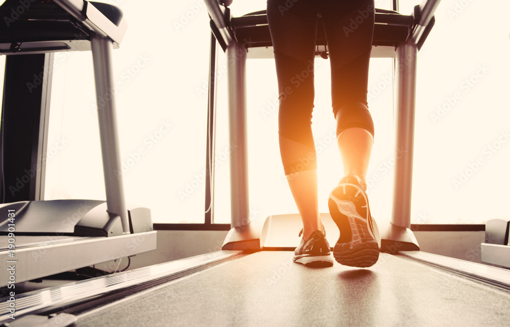 Φωτογραφία Lower body at legs part of Fitness girl running on running machine or treadmill in fitness gym with sun ray