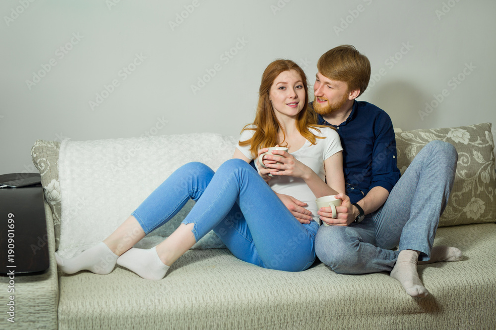 beautiful young couple guy with a girl with red hair sitting on the couch and drinking tea beautiful young couple guy with a girl with red hair sitting on the couch and drinking tea