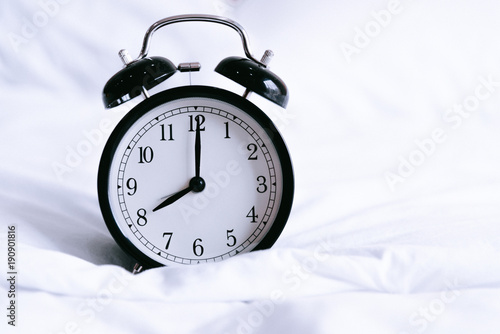 Black alarm clock on white bed. Time and hours concept. Interior and object theme