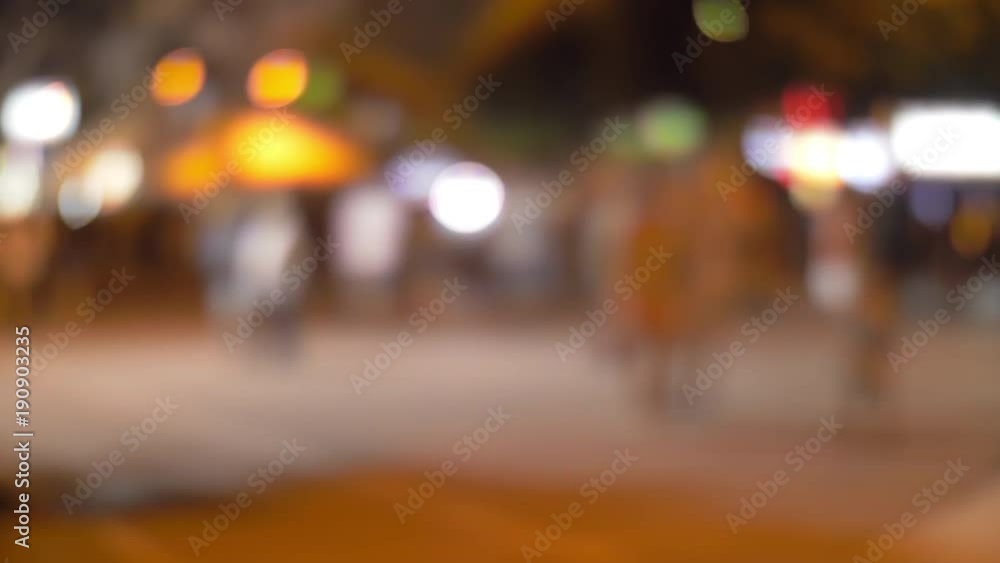 Defocused shot of people walking in the street illuminated at night with colorful lights Defocused shot of people walking in the street illuminated at night with colorful lights