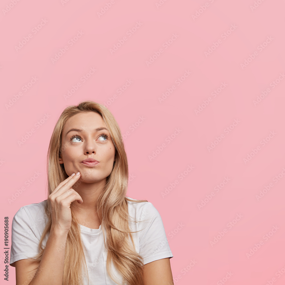 Φωτογραφία Adorable thoughtful blonde woman looks upwards, poses against pink background with copy space for your promotional text or advertisment