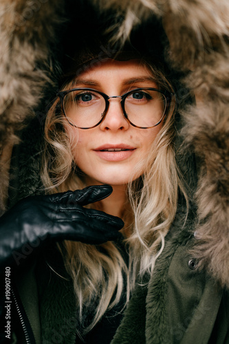 Eccentric female in glasses and hat portrait. Funny young beautiful girl fooling . Beautiful artistic model in jacket with faux fur making funny faces. Old fashioned style aristocrat bizarre woman.