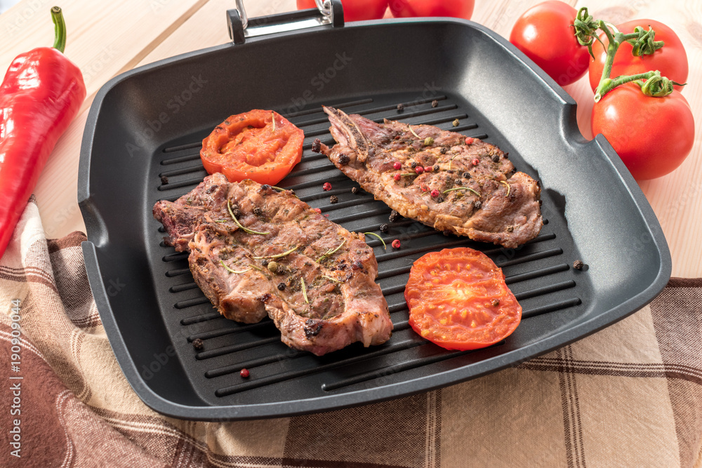 Grilled steak on grill pan with tomatoes on wooden background