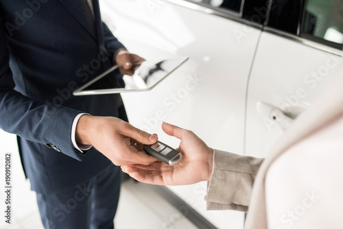 High angle close up of car salesman giving keys to client standing next to white luxury car, copy space
