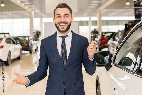 Photography Portrait of handsome car salesman a holding car keys and smiling cheerfully at c