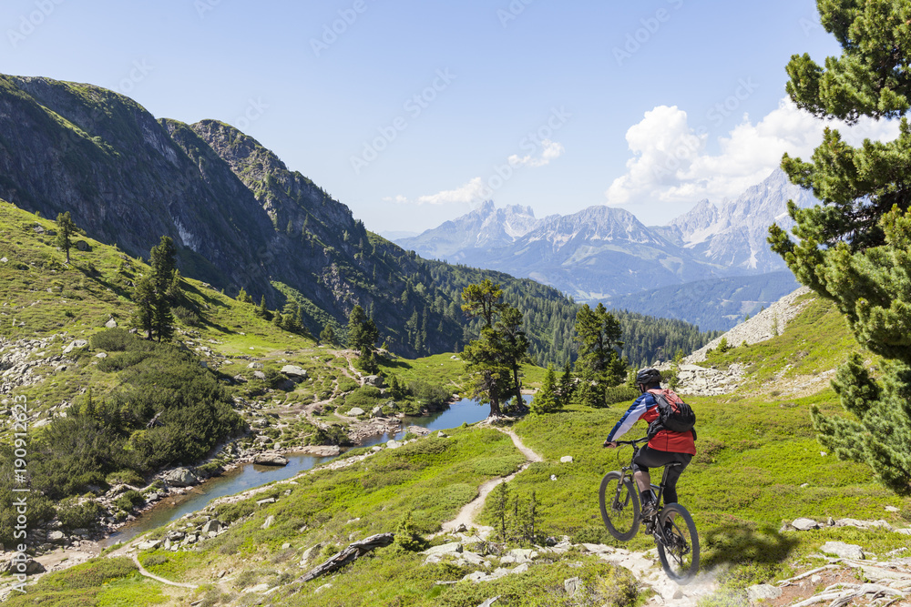 Mountainbiker downhill on Reiteralm with mountain Dachstein in Styria Austria