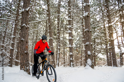 Cyclist in Red Riding Mountain Bike in Beautiful Winter Forest. Adventure, Sport and Enduro Cycling Concept.