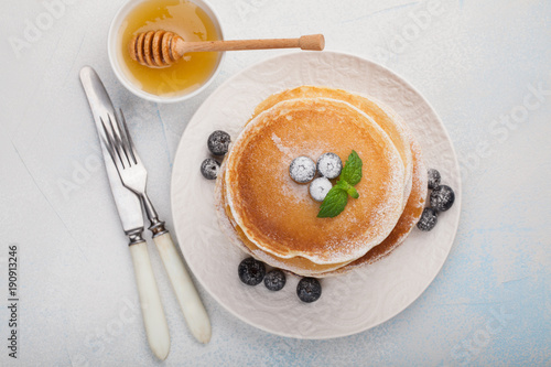 A stack of delicious pancakes with honey and blueberries on a light blue background. Top view with copy space photo