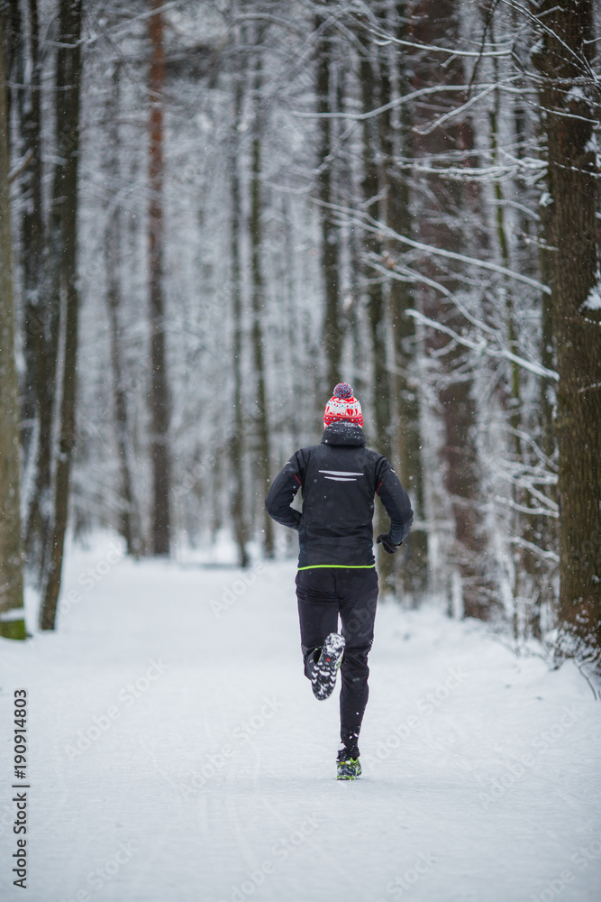 Photo from back of running athlete among trees in winter forest