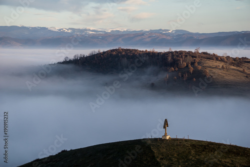 A christian cross on a hilltop overlooking a misty valley below