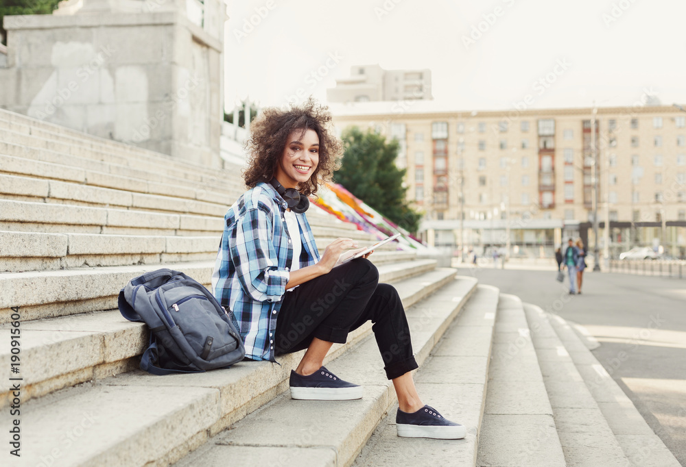 Smiling student sitting on stairs using tablet Smiling student sitting on stairs using tablet