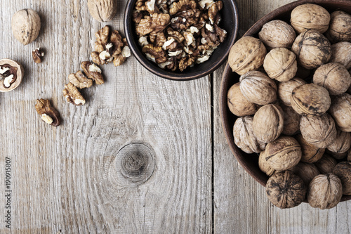 Walnut kernels in a bowl and whole walnuts on table.
