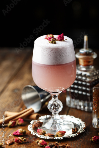 pink cocktail with foam, decorated with pink buds, on the bar.