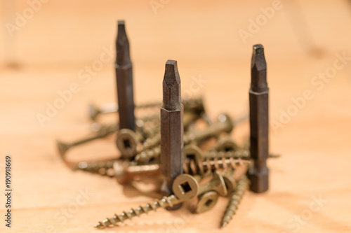 Bits for screwdrivers along with several screws placed on a wooden board. Set of heads for screwdriver (bits). Tools collection of drywall screws on wooden background, with selective focus. photo