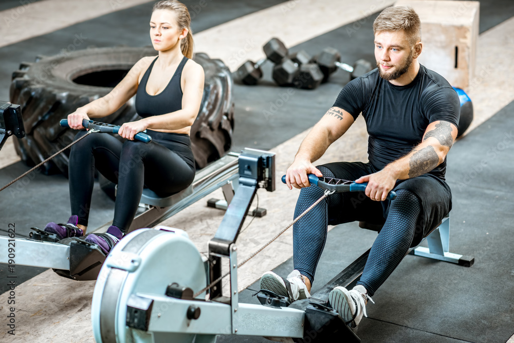 Young and beautiful couple training with exercise rowing machines in the gym Young and beautiful couple training with exercise rowing machines in the gym