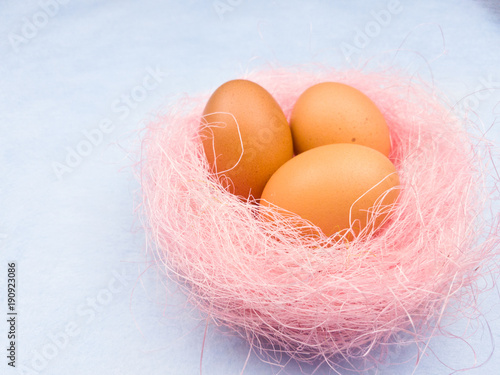 Yellow easter eggs in pink nest on pastel blue background. Close up.