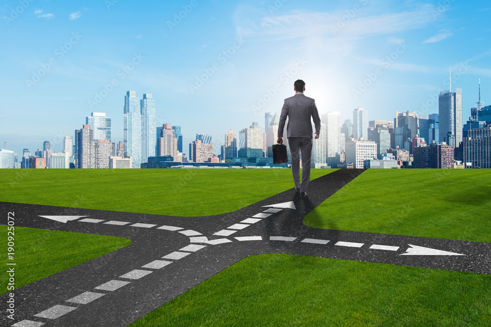 Young businessman at crossroads in uncertainty concept Young businessman at crossroads in uncertainty concept