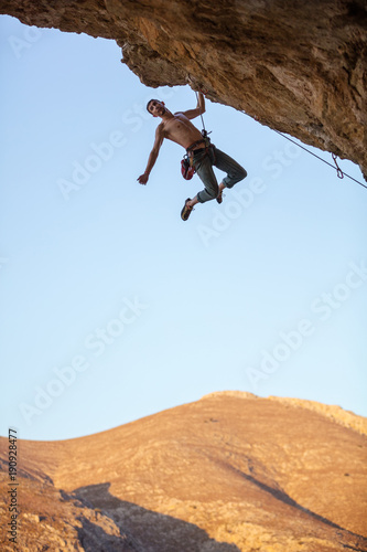 Male rock climber hanging with one hand on cliff