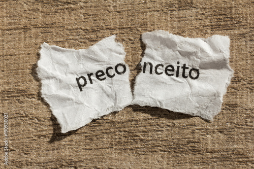 фотографія Torn paper written preconceito, portuguese word for prejudice, over wood table