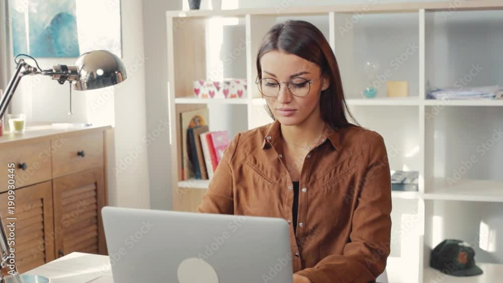 Young woman with straight hair typing on laptop keyboard in nice sunny room. Happy Caucasian girl looking at camera, smiling. Coziness. Indoors. Young woman with straight hair typing on laptop keyboard in nice sunny room. Happy Caucasian girl looking at camera, smiling. Coziness. Indoors.