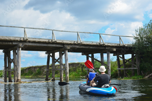 Happy coulple kayaking on the river on the background of old wooden bridge. Extreme summer sports concept. photo