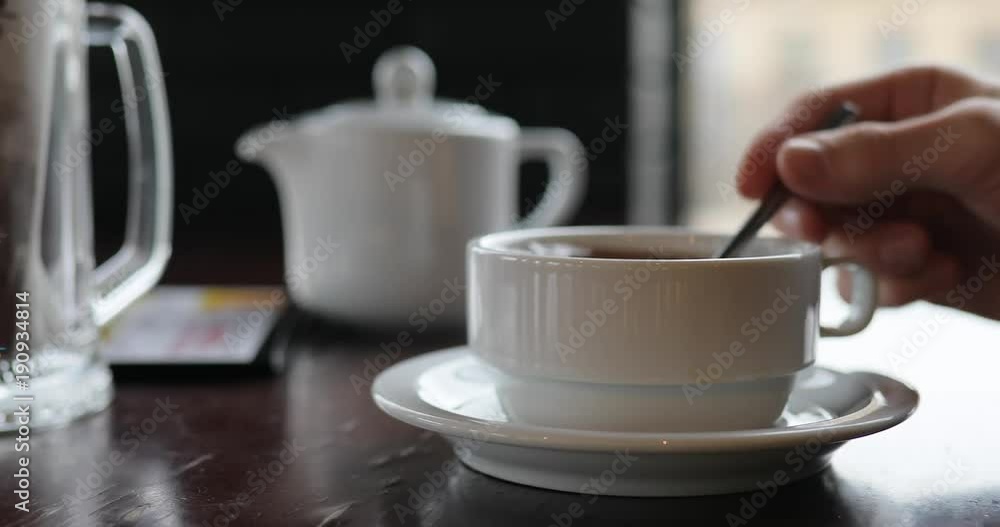 Person hand mixing sugar in a tea cup and drinking beverage Person hand mixing sugar in a tea cup and drinking beverage