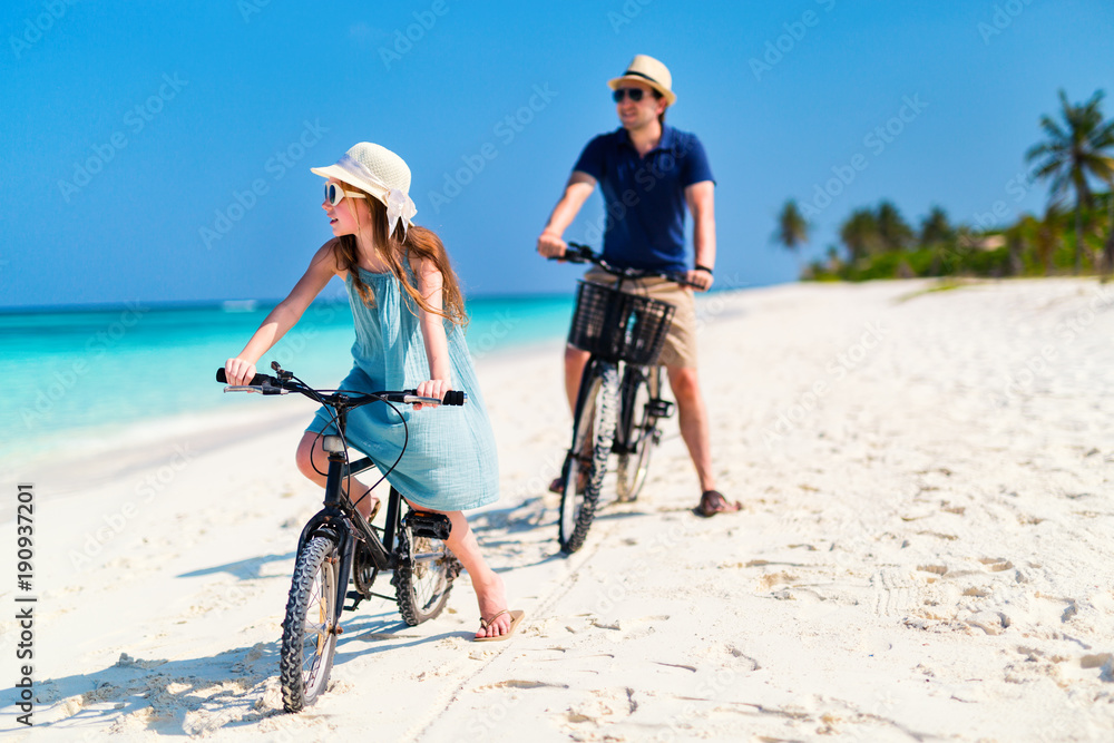 Fototapeta premium Father and daughter riding bikes at tropical beach
