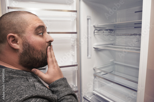 Surprised funny fat man looking into empty fridge