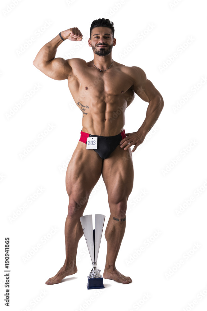 Handsome winning bodybuilder next to his cup, shirtless bodybuilder man, standing, in studio shot, looking at camera, isolated on white