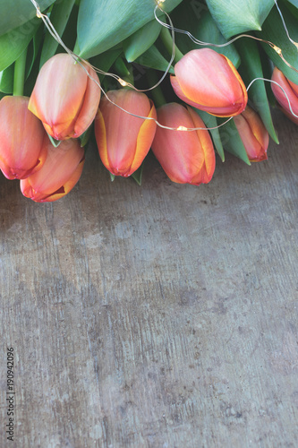 View of a beautiful bouquet of orange and yellow tulips decorated with led lights chain on old, rustic wooden background