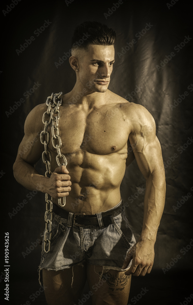 Good Looking Young Gym Fit Man Showing His Sexy Six Pack Abs While Carrying  Iron Chain on one Shoulder, on Dark Background. Stock Photo | Adobe Stock