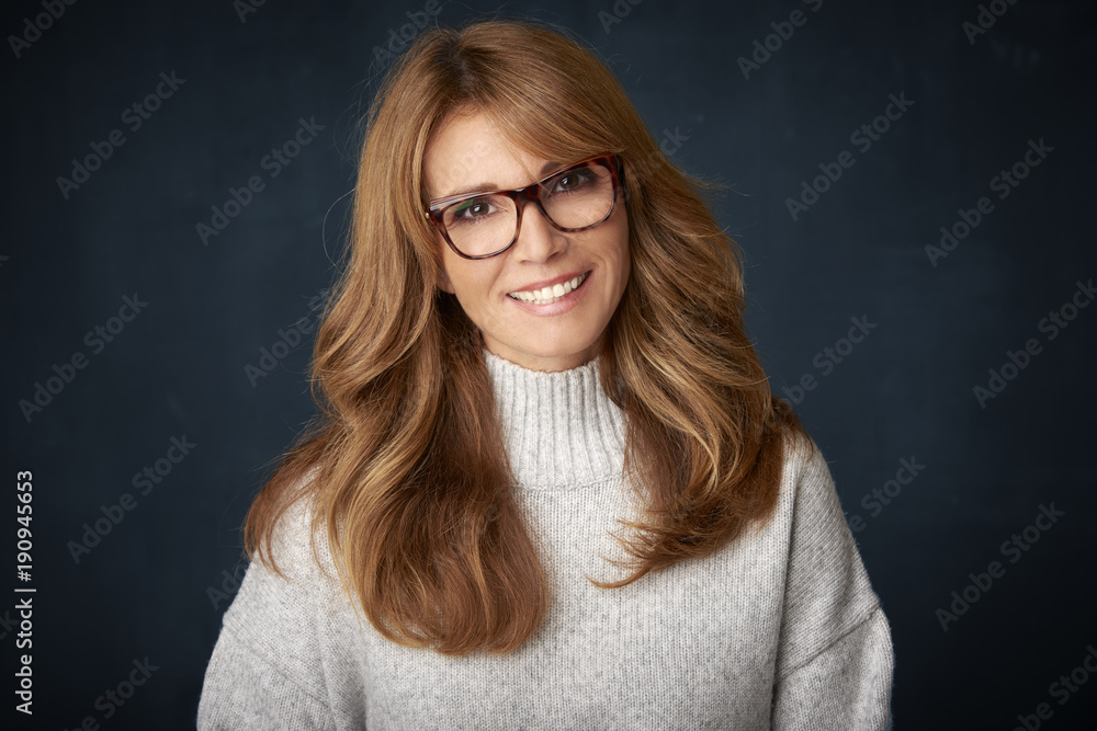 Beautiful smiling mature woman portrait. Happy woman wearing turtle neck sweater and looking confidently at camera while posing at dark backgorund. Beautiful smiling mature woman portrait. Happy woman wearing turtle neck sweater and looking confidently at camera while posing at dark backgorund.