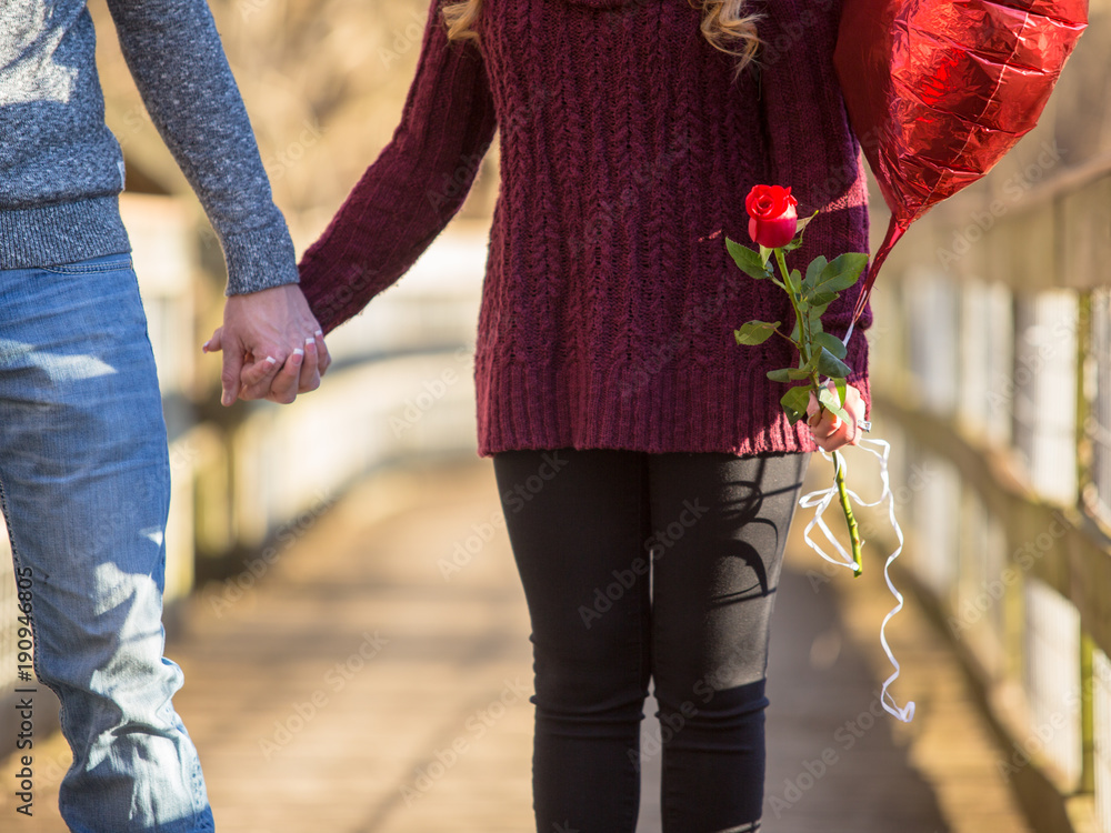 Obraz premium Couple walking holding hands no faces. She holds a red balloon and a red rose.