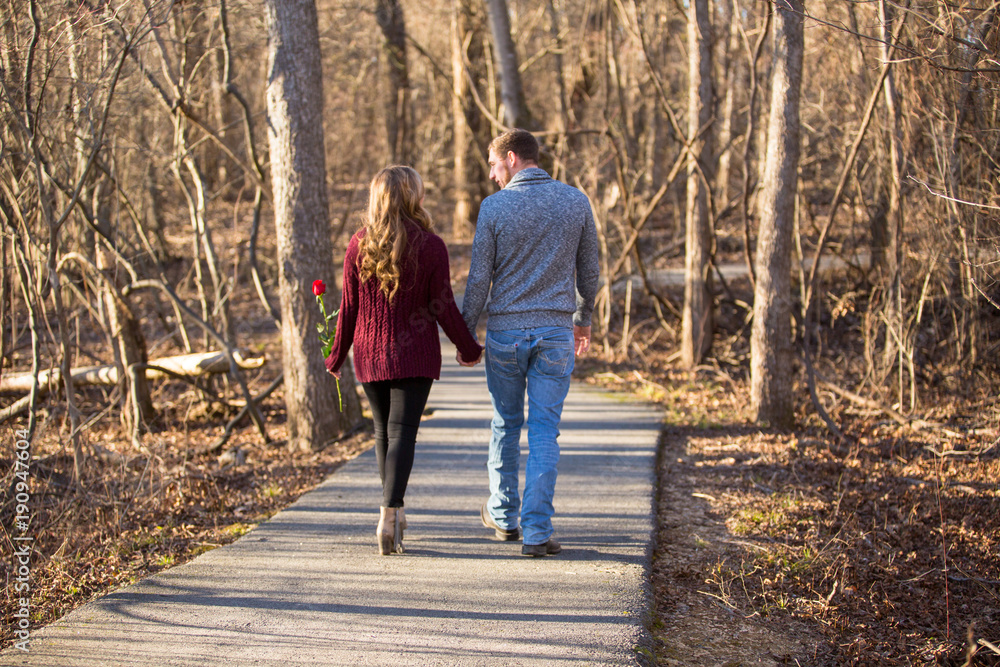 Couple walking away from viewer holding hands she has a red rose Couple walking away from viewer holding hands she has a red rose