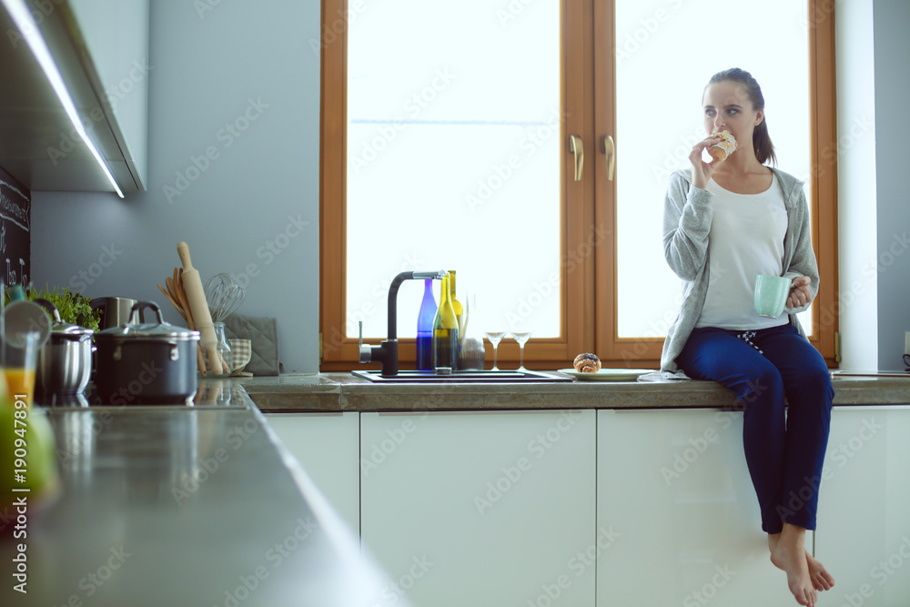 Obraz premium Beautiful young woman using a digital tablet in the kitchen.