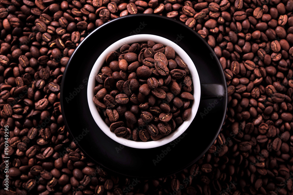 Black coffee cup and saucer one single for espresso or capuccino filled full of coffee beans on a background of scattered dark coffee beans photo Black coffee cup and saucer one single for espresso or capuccino filled full of coffee beans on a background of scattered dark coffee beans photo