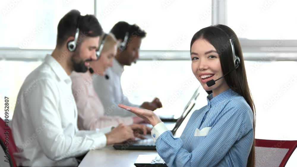 Asian girl in office praising her colleagues. Young asian office girl pointing palm up at colleagues behind. Asian girl in office praising her colleagues. Young asian office girl pointing palm up at colleagues behind.