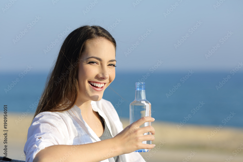 Happy woman holding a water bottle and looking at you outdoors Happy woman holding a water bottle and looking at you outdoors