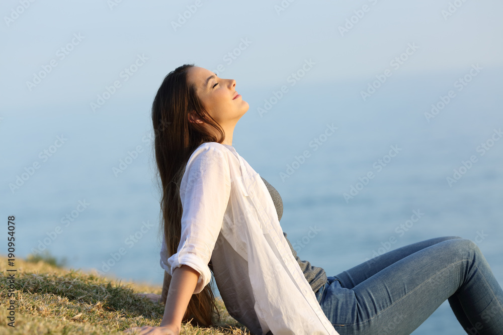 Relaxed woman breathing fresh air sitting on the grass